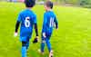 Two MK United U8 players talking and walking off the pitch in wet conditions